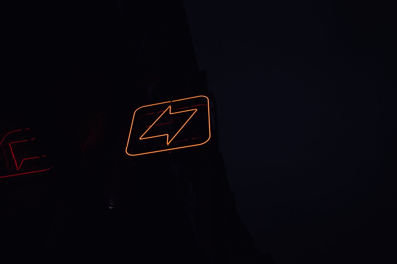 hero-img-01 A glowing neon lightning bolt sign against a dark night background, symbolizing energy and electricity.